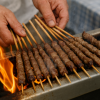 Arrosticini sulla griglia con fiamme e mani che li girano