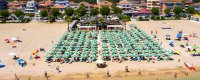Una spiaggia affollata con file di ombrelloni verdi e lettini.