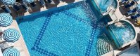 Una piscina rettangolare con bordi chiari e ombrelloni a righe blu.