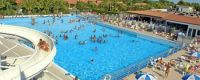 Una grande piscina con scivolo e molte persone che nuotano, circondata da sdraio.