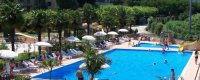 Piscina rettangolare circondata da ombrelloni e palme, con poche persone in acqua.