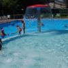 Bambini che giocano in piscina con una fontana centrale.