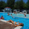 Persone nuotano in piscina, una donna prende il sole sul bordo.