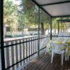 Veranda di legno coperta con tavolo e sedie bianche, circondata da alberi.