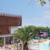 Una piscina esterna con palme, un edificio moderno a sinistra e un cartello di benvenuto colorato.