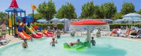 Bambini che giocano in una piscina con scivoli colorati e ombrelloni sullo sfondo.