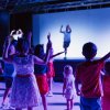 Bambini che danzano di fronte a un palco illuminato di blu.