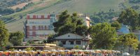 Spiaggia gremita di persone, ombrelloni gialli e colline verdi dietro.