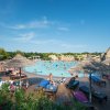 Spiaggia affollata con piscina, lettini e ombrelloni di paglia.