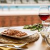 Tavola apparecchiata con piatto di cibo e bicchiere di vino rosso vicino a una piscina.