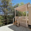 Una veranda in legno chiaro con scale, circondata da alberi, sotto un cielo azzurro.