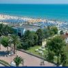Spiaggia attrezzata con ombrelloni vicino a una passeggiata con palme e strutture.