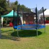 Un prato con trampolino blu e tende con tavoli e sedie rosse.