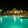 Piscina illuminata di notte con persone sedute sotto gazebo.