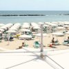 Spiaggia con ombrelloni bianchi e lettini verdi vicino al mare.