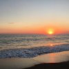 Tramonto sul mare, con il sole che cala all'orizzonte e onde che lambiscono la spiaggia.