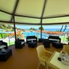 Area coperta con divani e tavolini, vista sul mare e una piscina con lettini arancioni sullo sfondo.