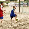 Bambini in maglie colorate giocano a calcio sulla sabbia vicino a una porta improvvisata.